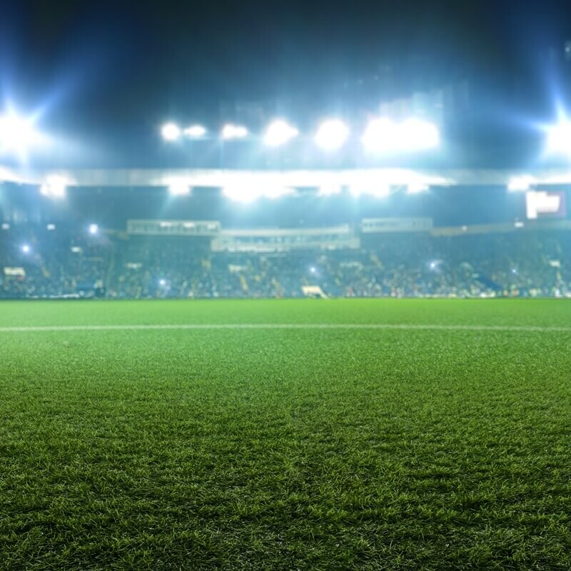 Illuminated football stadium at night, viewed from pitch level toward the stands.