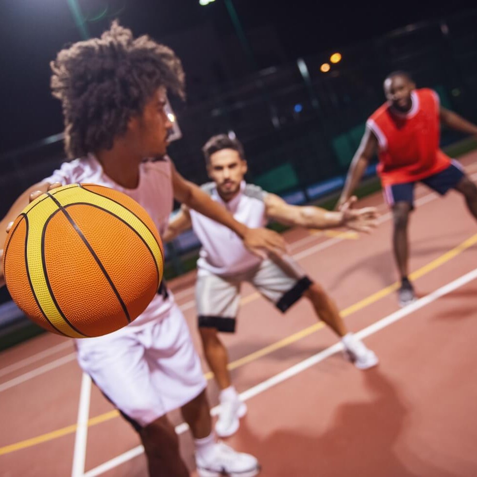 Men play basketball on an outdoor court at night.