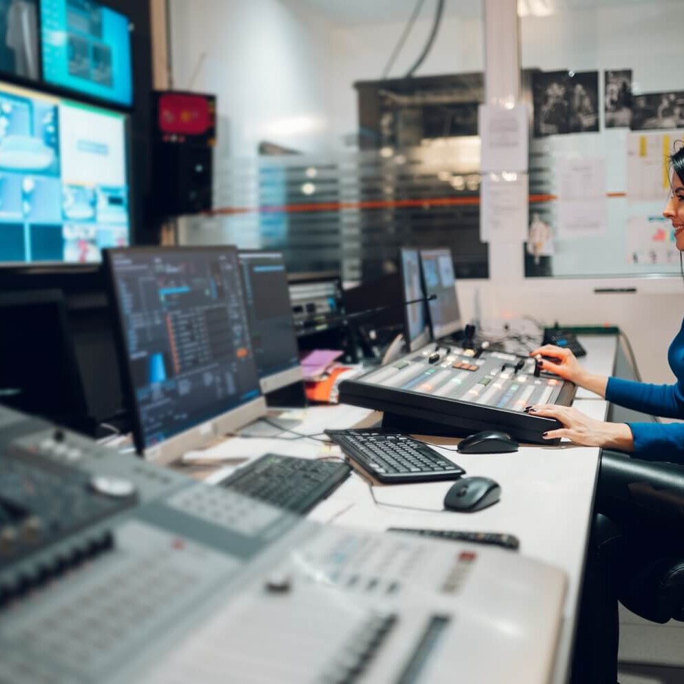 Broadcast operator working at a production console with multiple monitors in a professional control room.