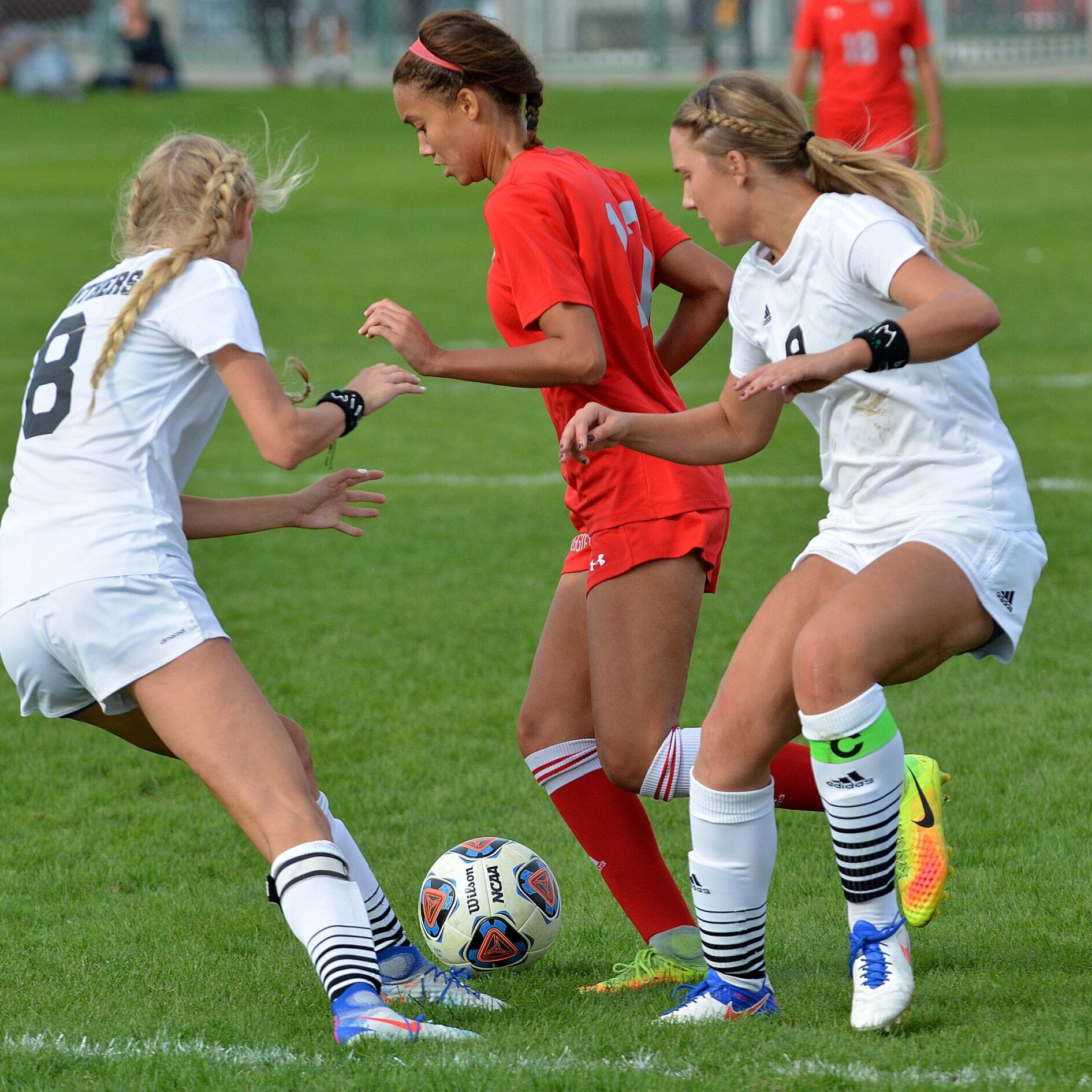 Female football players competing for the ball during a match on a grass pitch.